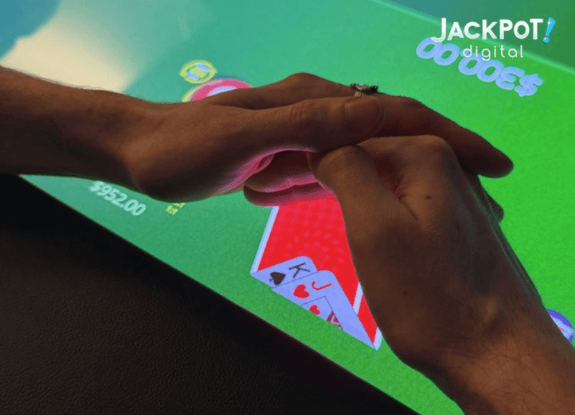 Hands touching a green-lit touchscreen poker table displaying playing cards and chip counts